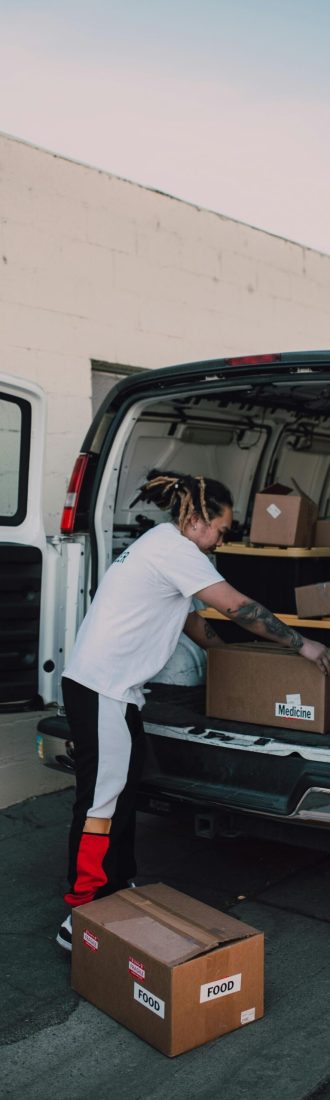 Tattooed volunteer arranging donation boxes in an open van, exuding community spirit outdoors.